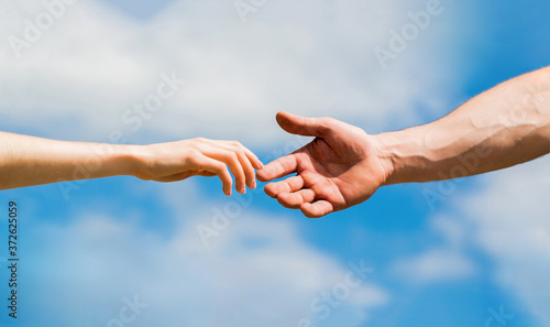 Hands of man and woman on blue sky background. Lending a helping hand. Solidarity, compassion, and charity, rescue. Hands of man and woman reaching to each other, support. Giving a helping hand © Yevhen
