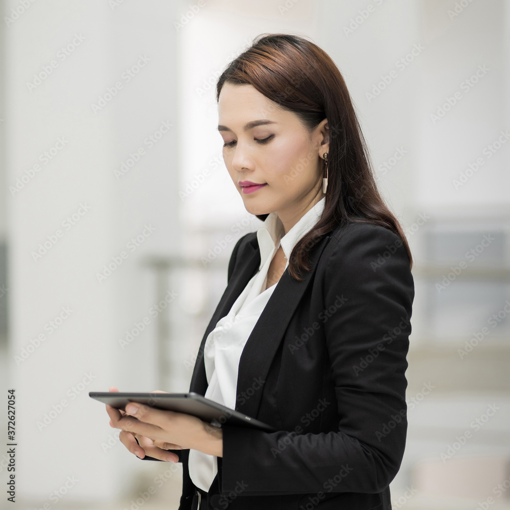 Portrait of a young cheerful businesswoman surfing social network on digital tablet in front of office during break. Asian business woman standing in office building. Stock photo Portrait of a young cheerful businesswoman surfing social network on digital tablet in front of office during break. Asian business woman standing in office building. Stock photo
