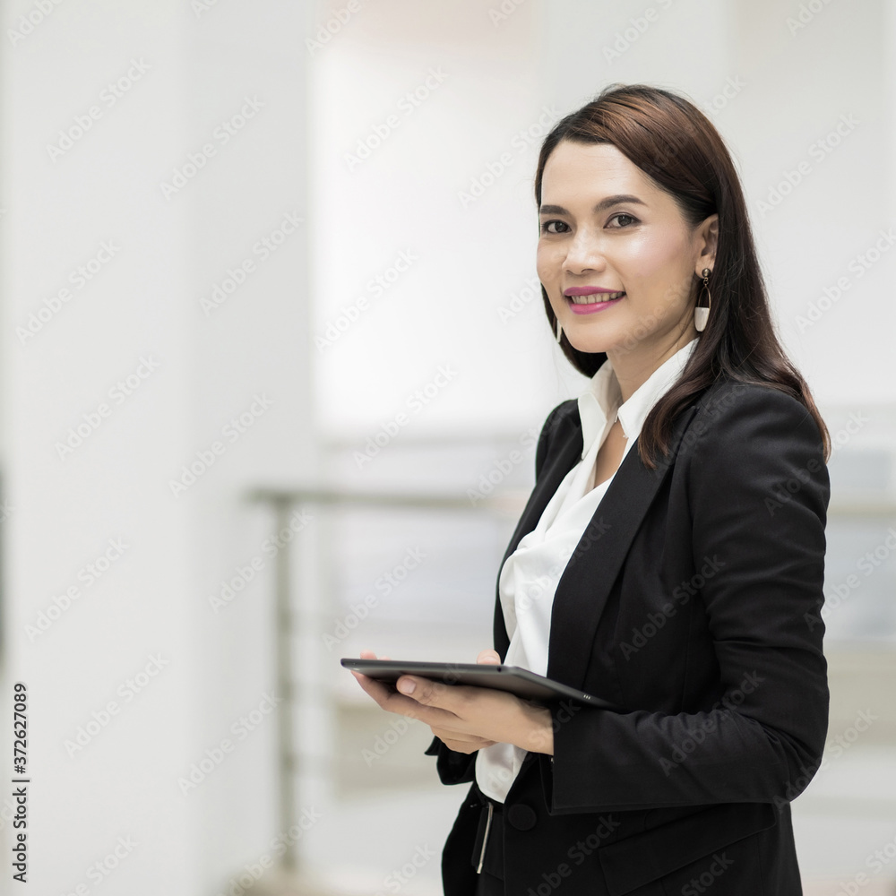 Portrait of a young cheerful businesswoman surfing social network on digital tablet in front of office during break. Asian business woman standing in office building. Stock photo Portrait of a young cheerful businesswoman surfing social network on digital tablet in front of office during break. Asian business woman standing in office building. Stock photo