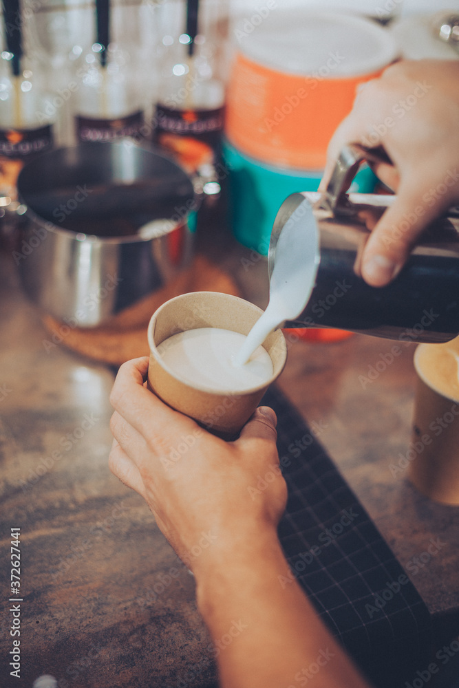 Barista pouring hot milk foam in to unbranded coffee paper cup Barista pouring hot milk foam in to unbranded coffee paper cup