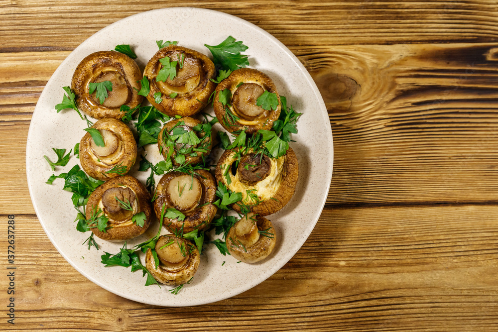 Baked mushrooms in plate on wooden table. Top view Baked mushrooms in plate on wooden table. Top view