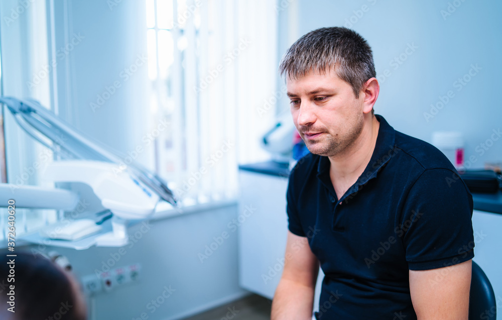Portrait of a male dentist gives consultation to a patient. Professional doctor on working place.