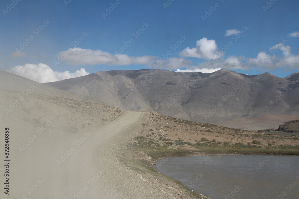View of the mountain and sand dune with dirt road in a sunny day, Tibet, China View of the mountain and sand dune with dirt road in a sunny day, Tibet, China