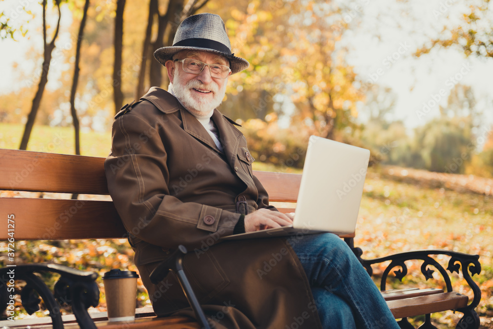 Photo of old man pensioner enjoy fall town park forest relax use laptop wifi modern connection type brows email sit bench wear cap headwear outerwear