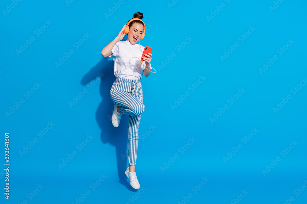 Full body photo of cheerful energetic girl jump enjoy listen music headset smartphone wear style stylish trendy white t-shirt isolated over bright shine color background Full body photo of cheerful energetic girl jump enjoy listen music headset smartphone wear style stylish trendy white t-shirt isolated over bright shine color background