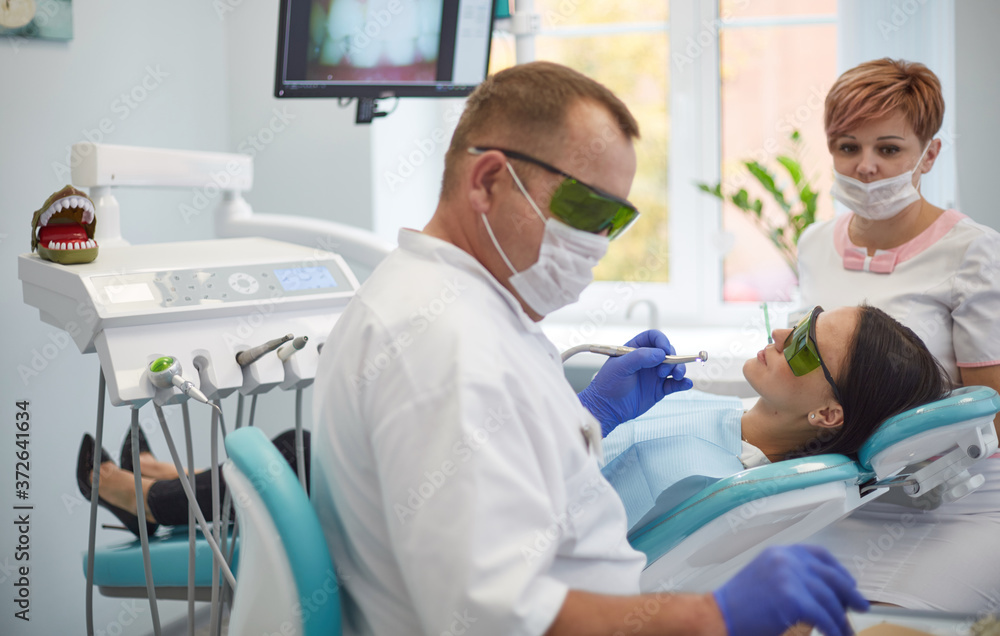 Obraz premium Doctor dentist treats teeth of a beautiful young girl patient. The girl on reception at the dentist. Doctor dentist treats tooth
