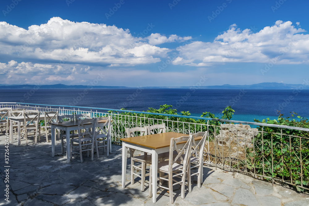 Chalkidiki, Greece empty tavern wooden chairs & table after new covid-19 measures. Restaurant outdoor seating area above the sea without customers in Kallithea, Kassandra peninsula.