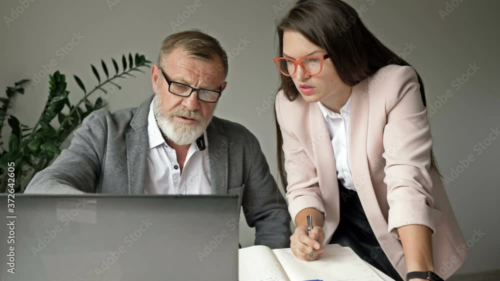 Two business partners work together in the office. Senior man discussing work with her young female colleague. Two business partners work together in the office. Senior man discussing work with her young female colleague.
