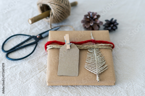 Ein Geschenkpaket weihnachtlich verpackt mit roter Schnur auf einem Leinen Tischtuch. Nahaufnahme, golden, Schere.