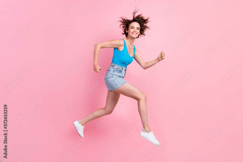 Full body size profile photo of charming pretty sporty young girl hold fists run against wind morning wear denim mini skirt blue singlet sneakers isolated pink color background