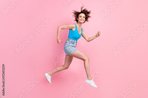 Full body size profile photo of charming pretty sporty young girl hold fists run against wind morning wear denim mini skirt blue singlet sneakers isolated pink color background