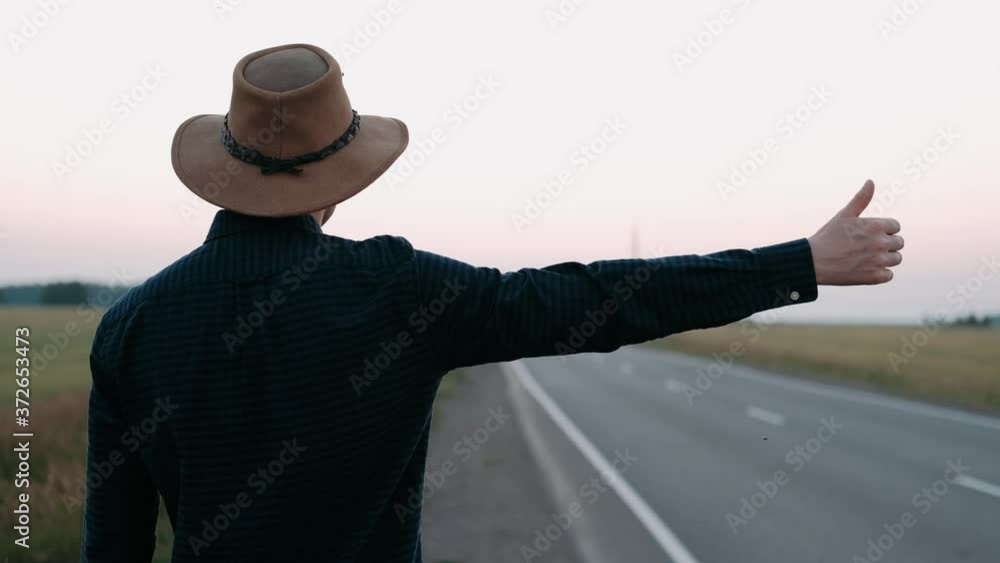 Man hitchhiking in a rural area next to the road. Hitchhiking. Traveler. Transportation Man hitchhiking in a rural area next to the road. Hitchhiking. Traveler. Transportation