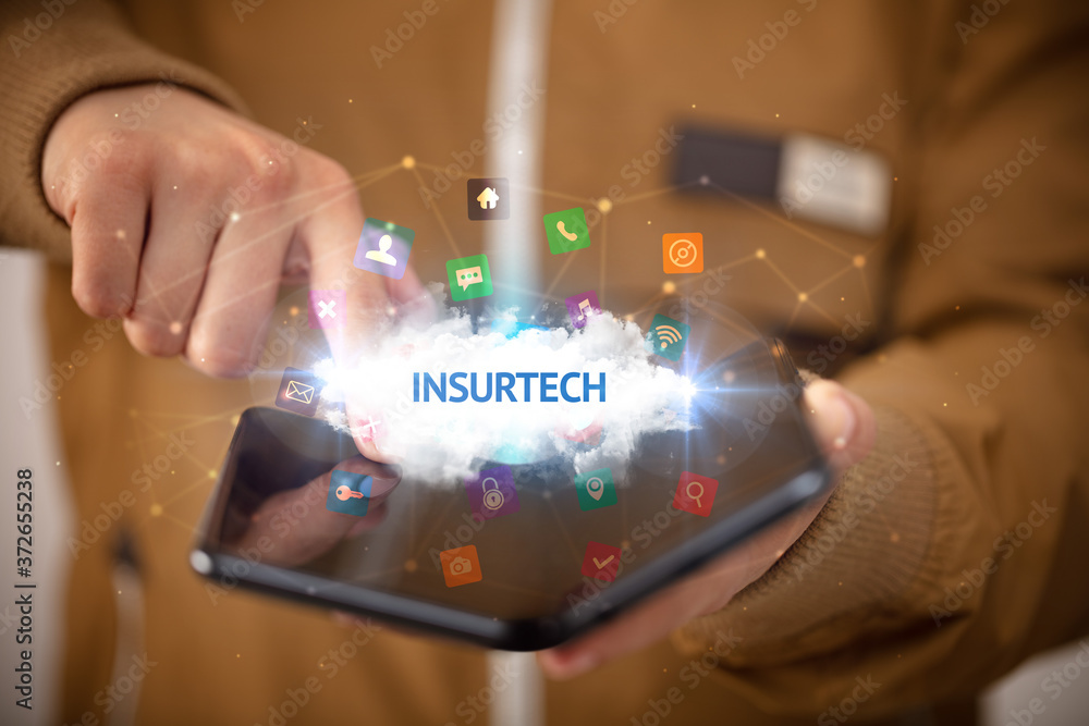 Businessman holding a foldable smartphone with INSURTECH inscription, technology concept Businessman holding a foldable smartphone with INSURTECH inscription, technology concept
