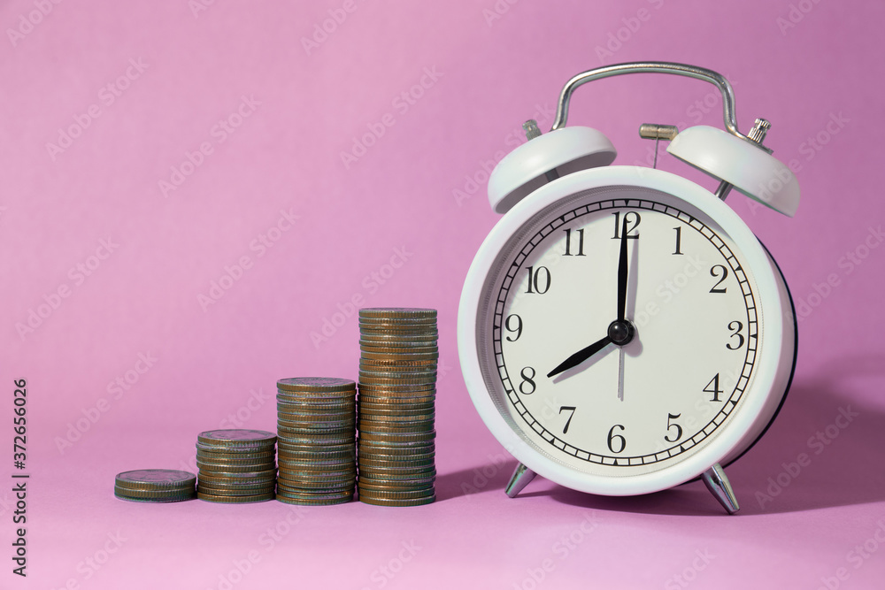 Coin pile stacked with alarm time clock with sweet pink space background for times to saving money concept. Coin pile stacked with alarm time clock with sweet pink space background for times to saving money concept.