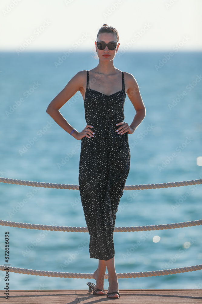 Fototapeta premium portrait of a beautiful brunette girl in a black dress on a sea background