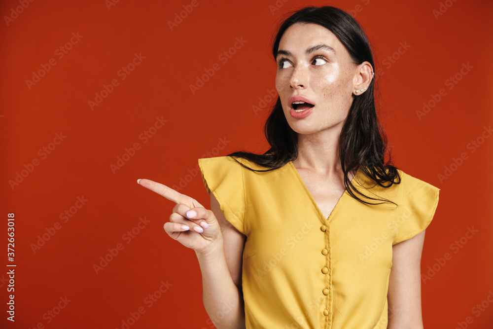 Image of young surprised woman pointing finger and looking aside Image of young surprised woman pointing finger and looking aside