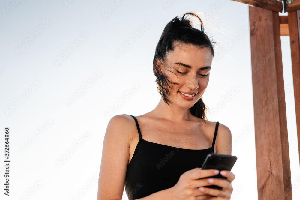 Fitness woman outdoors at the beach using mobile phone Fitness woman outdoors at the beach using mobile phone