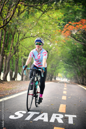 Fototapeta Naklejka Na Ścianę i Meble -  Start word and woman ride bike on road with tree tunnel, healthy lifestyle concept and sport motivation idea