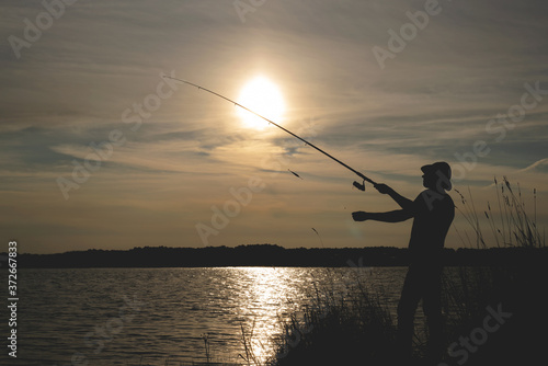 Fisherman silhouette with a rod on the pond. © Dmitriy