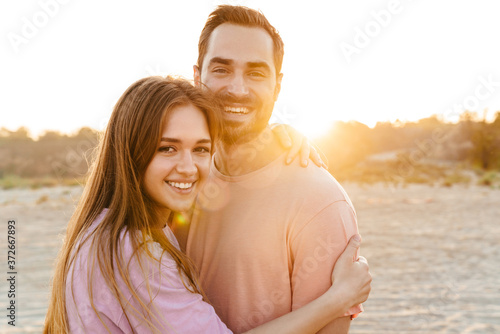Image of young caucasian happy couple smiling and hugging by seaside