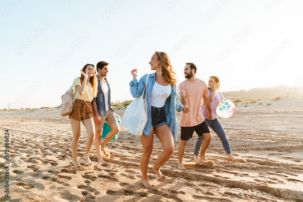 Image of young happy people smiling and walking together by seaside