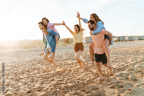 Image of young happy people having piggyback ride together by seaside