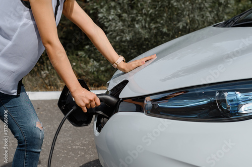 Close up hands holding a power cable and charging the battery of an electric car.