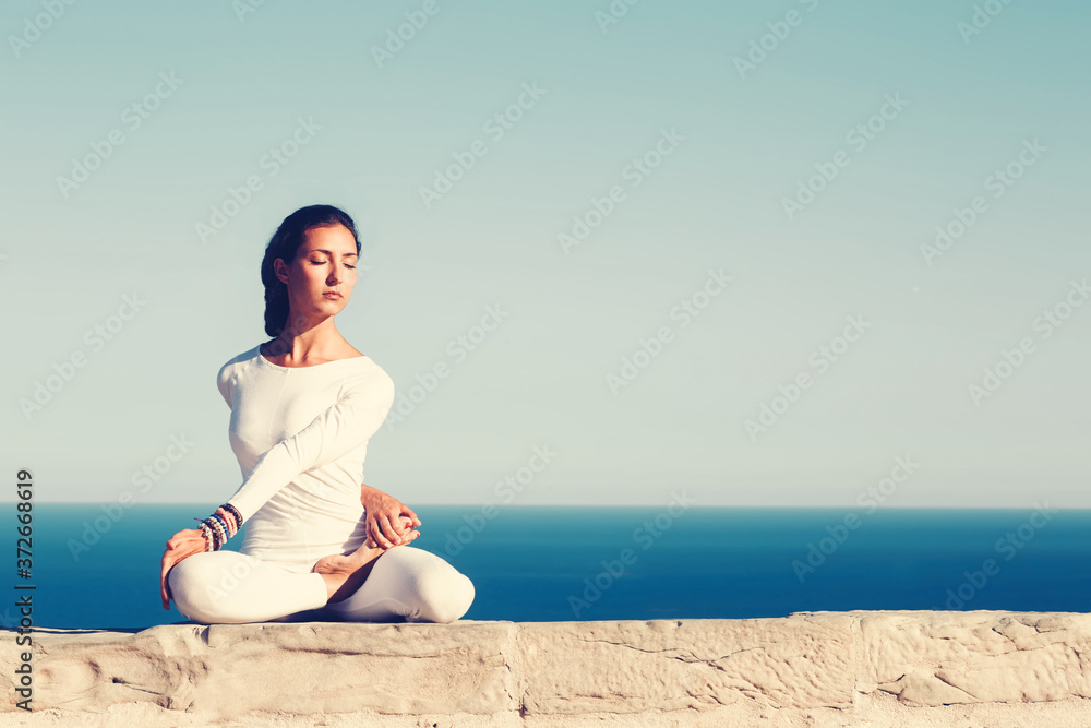 Front portrait of gorgeous young woman practicing yoga on a sunny day with amazing sea horizon on background, woman seeking enlightenment through meditation,relaxed girl performing yoga routine,filter