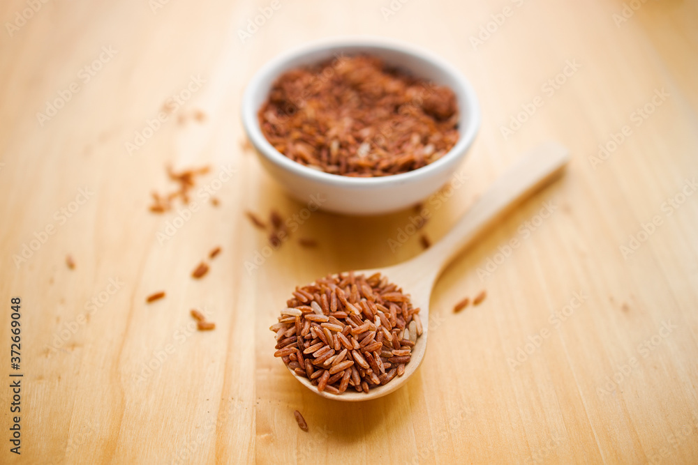 Closeup brown rice or red rice with wooden spoon and white ceramic bowl on wood table top. Healthy organic food concept. Closeup brown rice or red rice with wooden spoon and white ceramic bowl on wood table top. Healthy organic food concept.