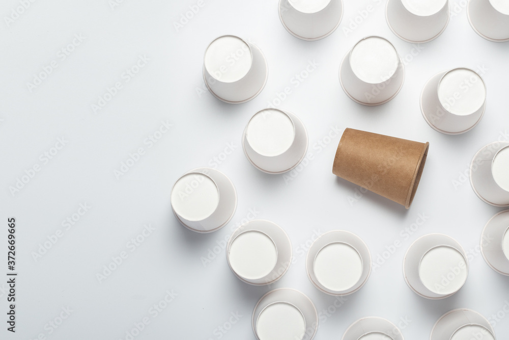 Many white and one brown paper cups, flipped upside down on a light background. Top view, flat lay. Many white and one brown paper cups, flipped upside down on a light background. Top view, flat lay.