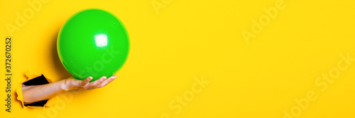 Female hand holding green inflatable ball on a bright yellow background. Banner photo