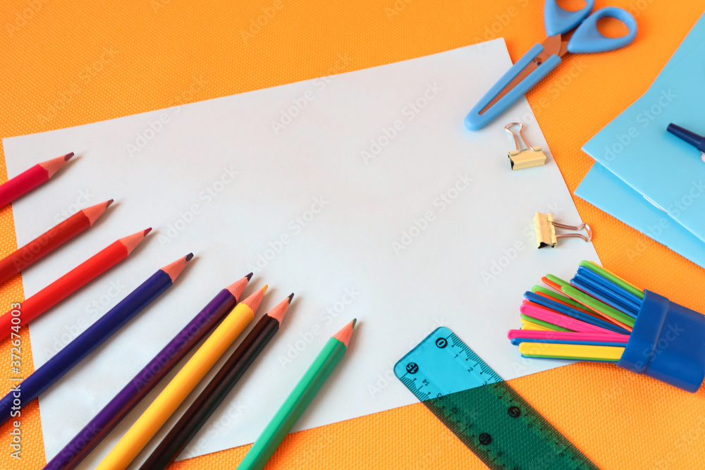 Colored pencils with school supplies on a yellow background, place for writing, top view