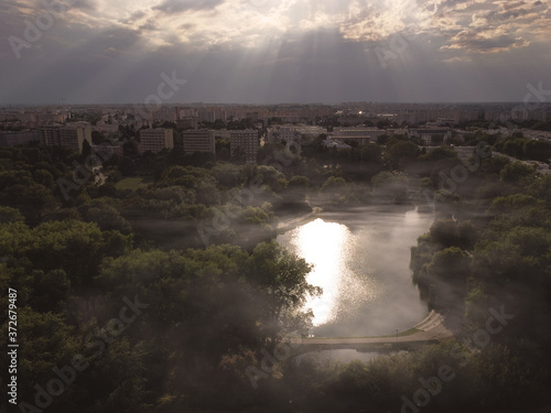 Beautifull view of park bathed in sunrays with little fog over a pond. Drone, aerial view