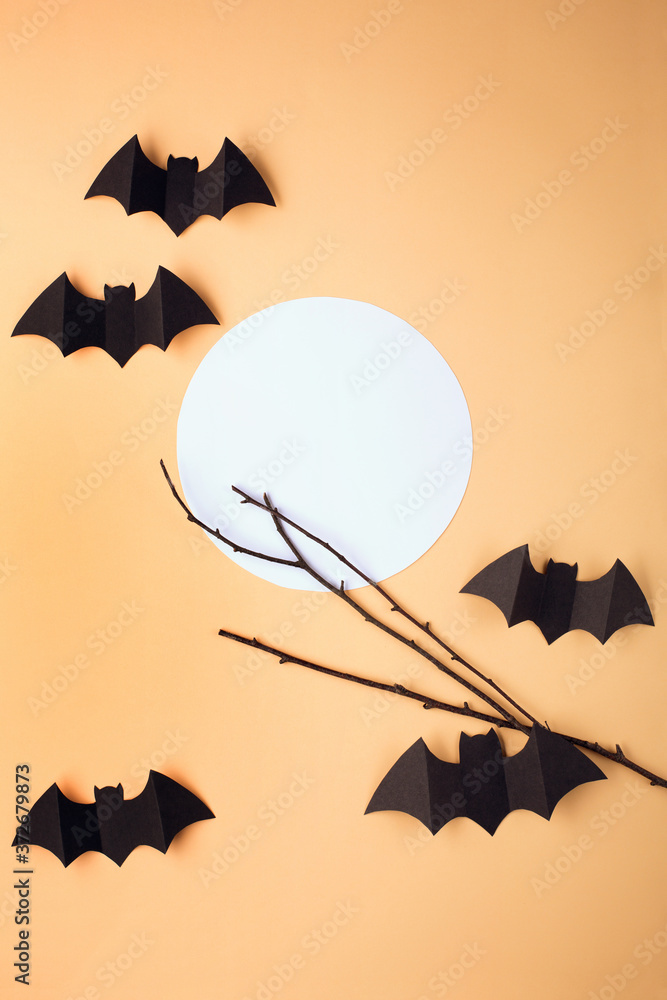 Halloween paper decorations on pastel beige background. Black bats, tree branch and moon. Halloween concept. Flat lay, top view, overhead. Minimal style. Halloween party greeting card mockup
