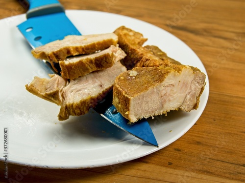 Sliced cured pork belly with blue knife on the white plate