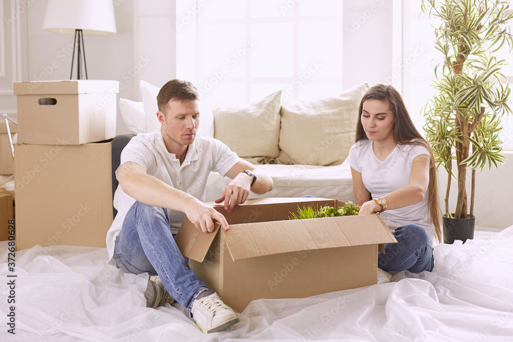 Portrait of happy couple looking at laptop computer together sitting in new house, surrounded with boxes Portrait of happy couple looking at laptop computer together sitting in new house, surrounded with boxes