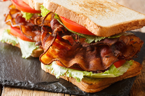 blt sandwich with crispy bacon, fresh iceberg salad and tomatoes close-up on a slate board on the table. horizontal photo