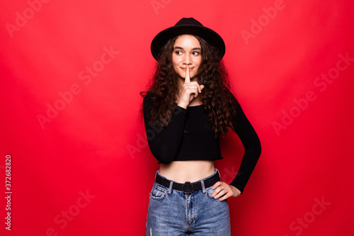 Young beautiful woman asking to be quiet with finger on lips standing over red background . Silence and secret concept.
