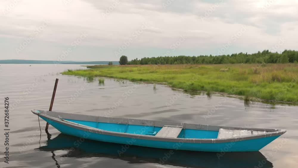 Old blue wooden boat anchored off the coast of the bay sways on calm waves. Little bird sitting on the bow of the boat. Tranquility morning by the river. Old blue wooden boat anchored off the coast of the bay sways on calm waves. Little bird sitting on the bow of the boat. Tranquility morning by the river.