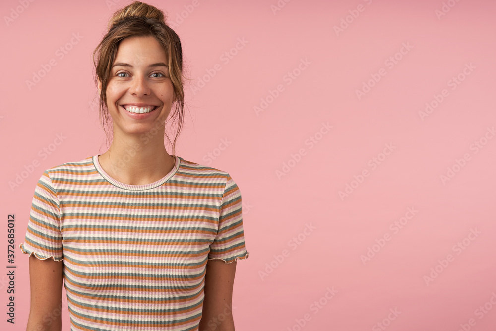 Indoor shot of young attractive brown haired female with casual hairstyle showing her white perfect tetth while looking gladly at camera, standing over pink background Indoor shot of young attractive brown haired female with casual hairstyle showing her white perfect tetth while looking gladly at camera, standing over pink background