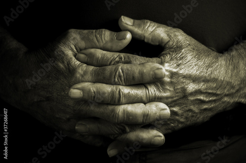 Elder senior adult with crossed wrinkled hands - black background