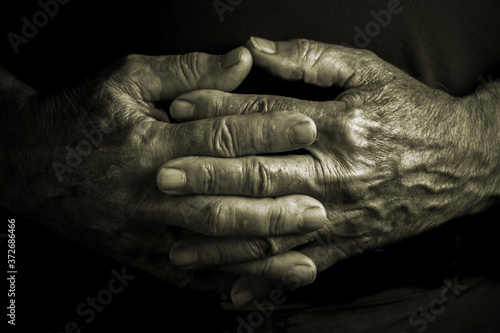 Elder senior adult with crossed wrinkled hands - black background