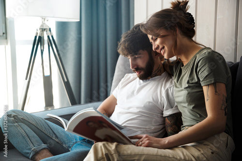 Fotografia Lovely young couple relaxing on a couch at home, reading magazine