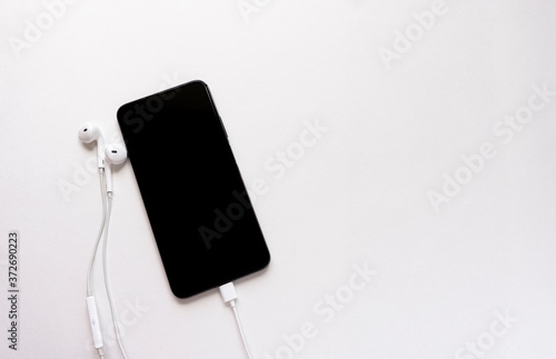 Headphones and smartphone on a white background. Ready to listen to music. Creative flat photography of desktop with headphones and mobile phone with text space