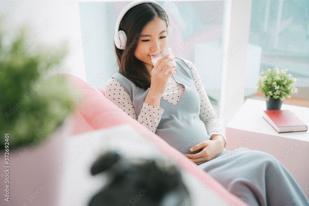 Young beautiful pregnant asian woman wearing headphone drinking milk. Young beautiful pregnant asian woman wearing headphone drinking milk.