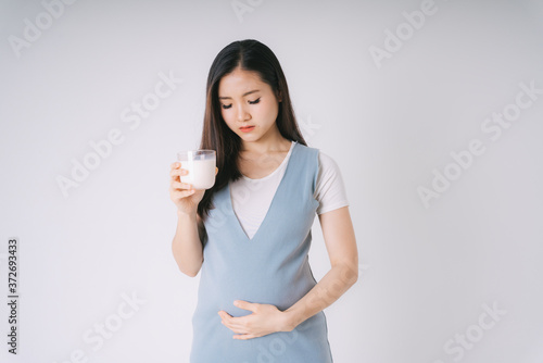 Beautiful pregnant asian woman holding a cup of fresh milk isolate over white background. © THESHOTS.CO