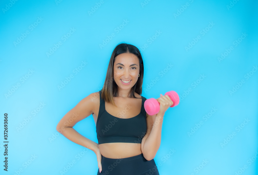 Beautiful woman in sport clothes with a dumbbell smiling