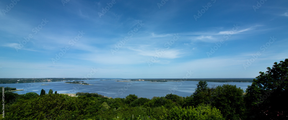 River landscape - a view from a high green bank to the bend of a wide large full-flowing river on a summer day