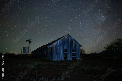 Milky Way stars above a rustic old barn and windmill at night