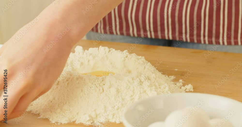 Closeup shot of a woman cracking eggs in a pile of flour. Making fresh pasta dough. Closeup shot of a woman cracking eggs in a pile of flour. Making fresh pasta dough.